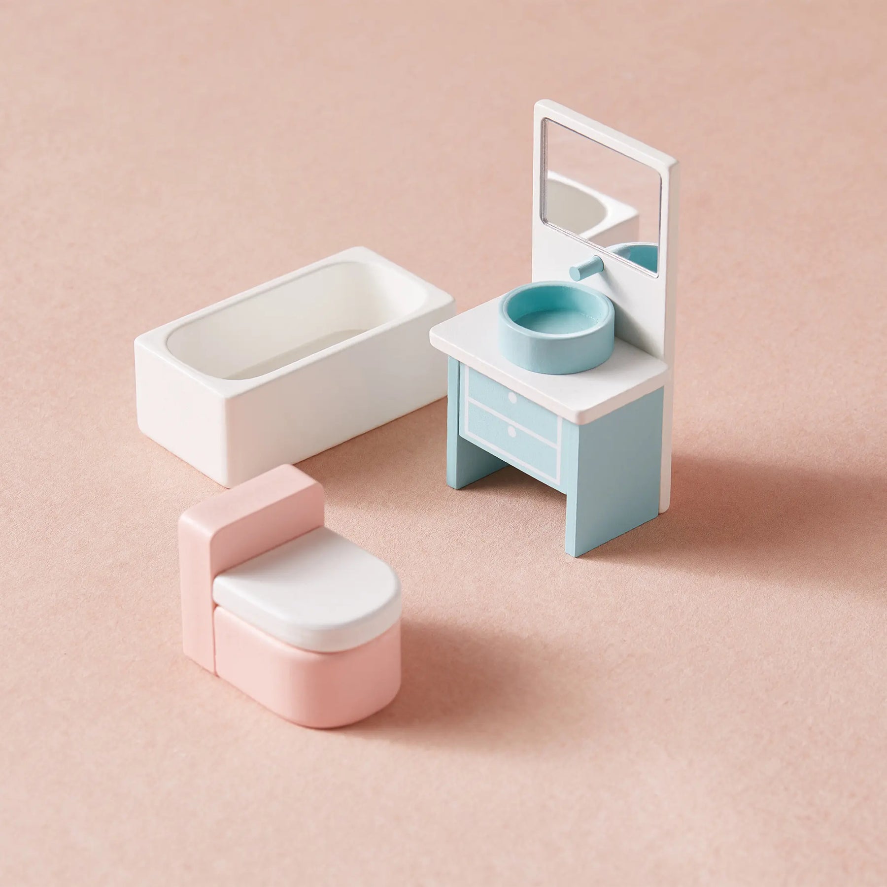 Mini pastel-colored dollhouse furniture set on a pink surface, featuring a white bathtub, pink and white toilet, and blue vanity—perfect for imaginative play in the Tiny Land® Sweetwood Love Dollhouse without Dolls by Tiny Land.