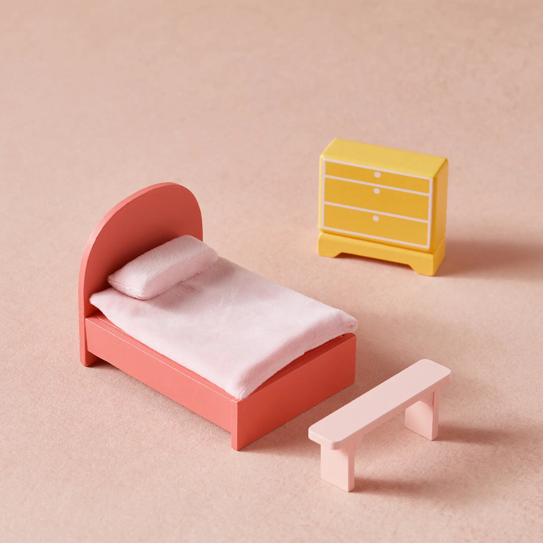 The Tiny Land® Sweetwood Love Dollhouse without Dolls by Tiny Land includes a pink bed with blanket, a yellow dresser with drawers, and a light pink bench—perfect for imaginative play, all arranged on a pale pink surface.