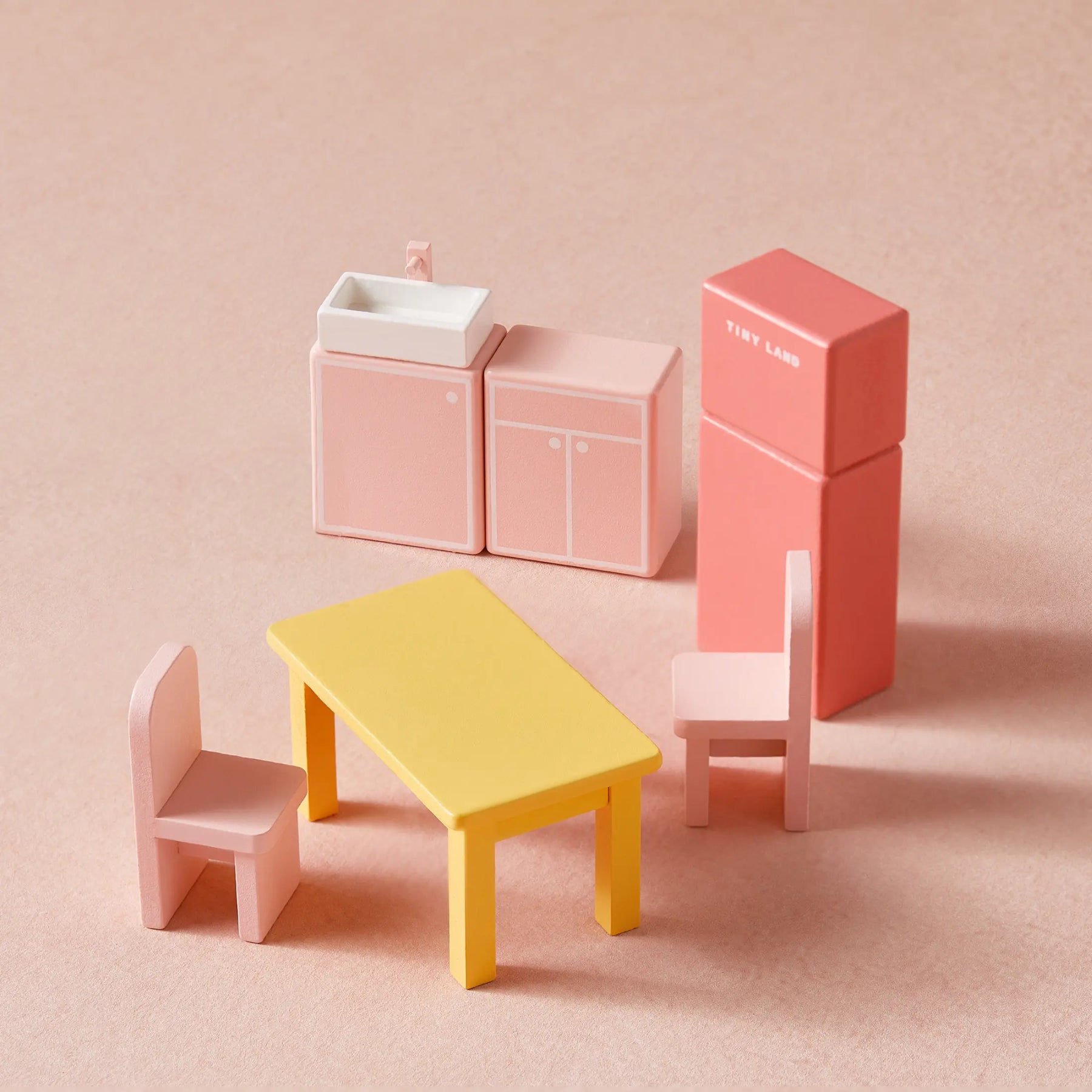 Tiny Land® Sweetwood Love Dollhouse Furniture Set features pink cabinets, a sink, coral fridge with Tiny Land branding, two pink chairs, and a yellow table—ideal for creative play in the Tiny Land Sweetwood Love Dollhouse.
