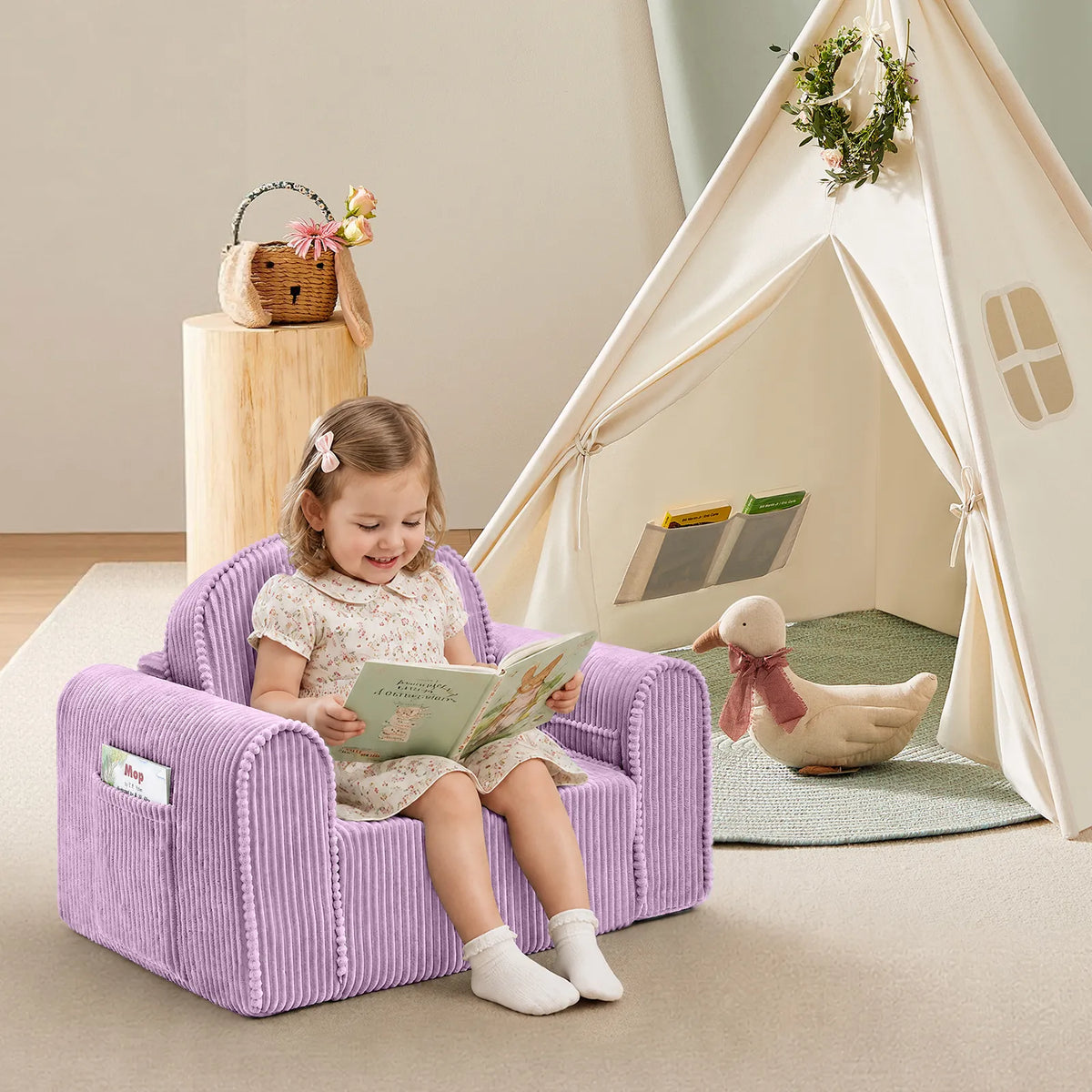 A young child sits on the Tiny Land® Ultimate Reading Retreat Corduroy Lounger, reading a book in a cozy, softly lit room. Nearby, the Premium Teepee from Tiny Land INC serves as an inviting Montessori-inspired kids’ reading nook, accompanied by a stuffed duck with a scarf and a basket on a small wooden table.|Purple