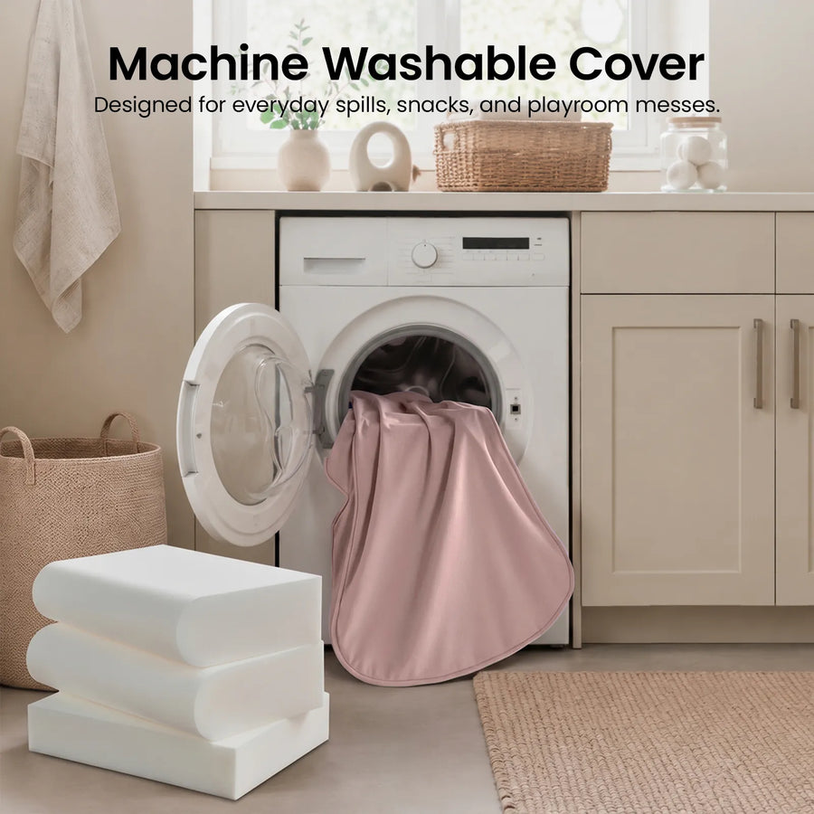 A pink cover from the Tiny Land® GentleSnug Kid Chair is being washed in a front-loading washing machine in a beige laundry room. Text above reads, Machine Washable Cover. Designed by Tiny Land for everyday spills, snacks, and playroom messes, this foldable kids chair makes cleanup after fun simple and convenient.|Pink