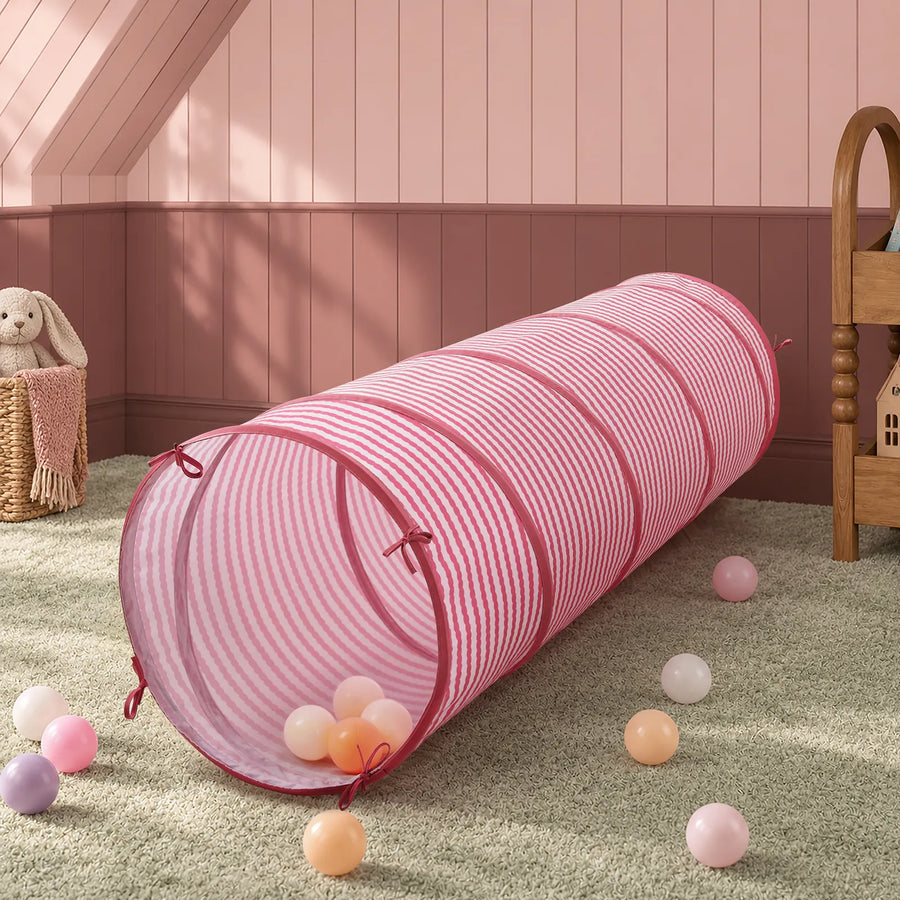 A cylindrical pink and white striped Tiny Land® Adventure Play Tunnel lying on a carpeted floor surrounded by small plastic play balls.|Pink