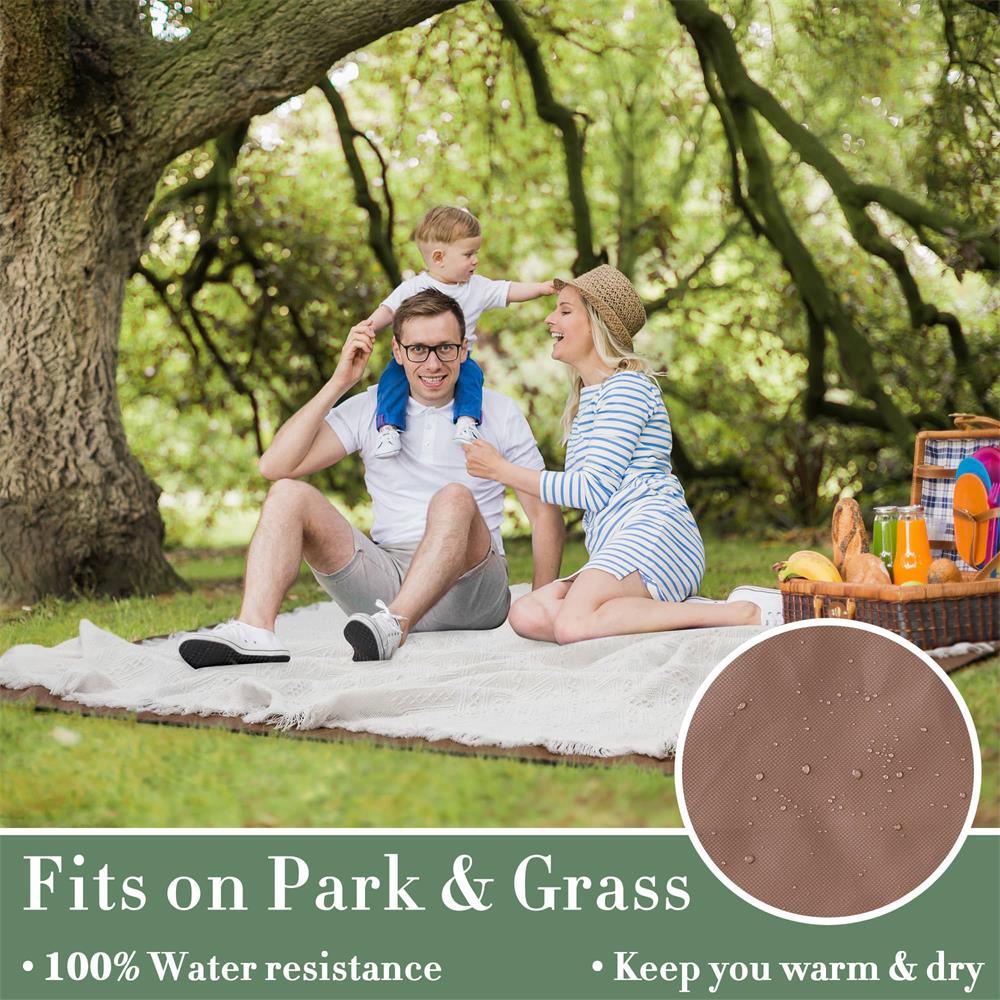 A smiling family enjoys a picnic on the Tiny Land® Picnic Blanket for Family under shady trees. A man with a child on his shoulders and a woman beside them relax on this 100% water-resistant blanket—perfect for parks and grass to keep you warm and dry.