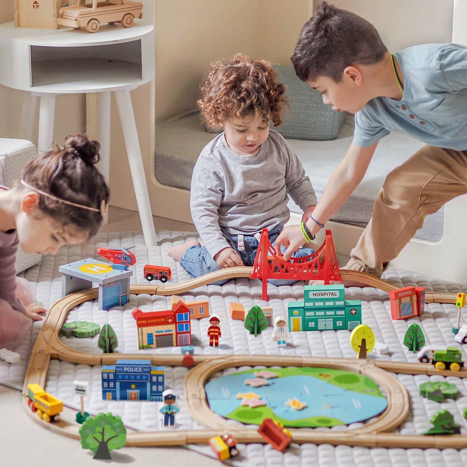 Three children sit on the playhouse mat, happily and intently playing with a wooden train track set.