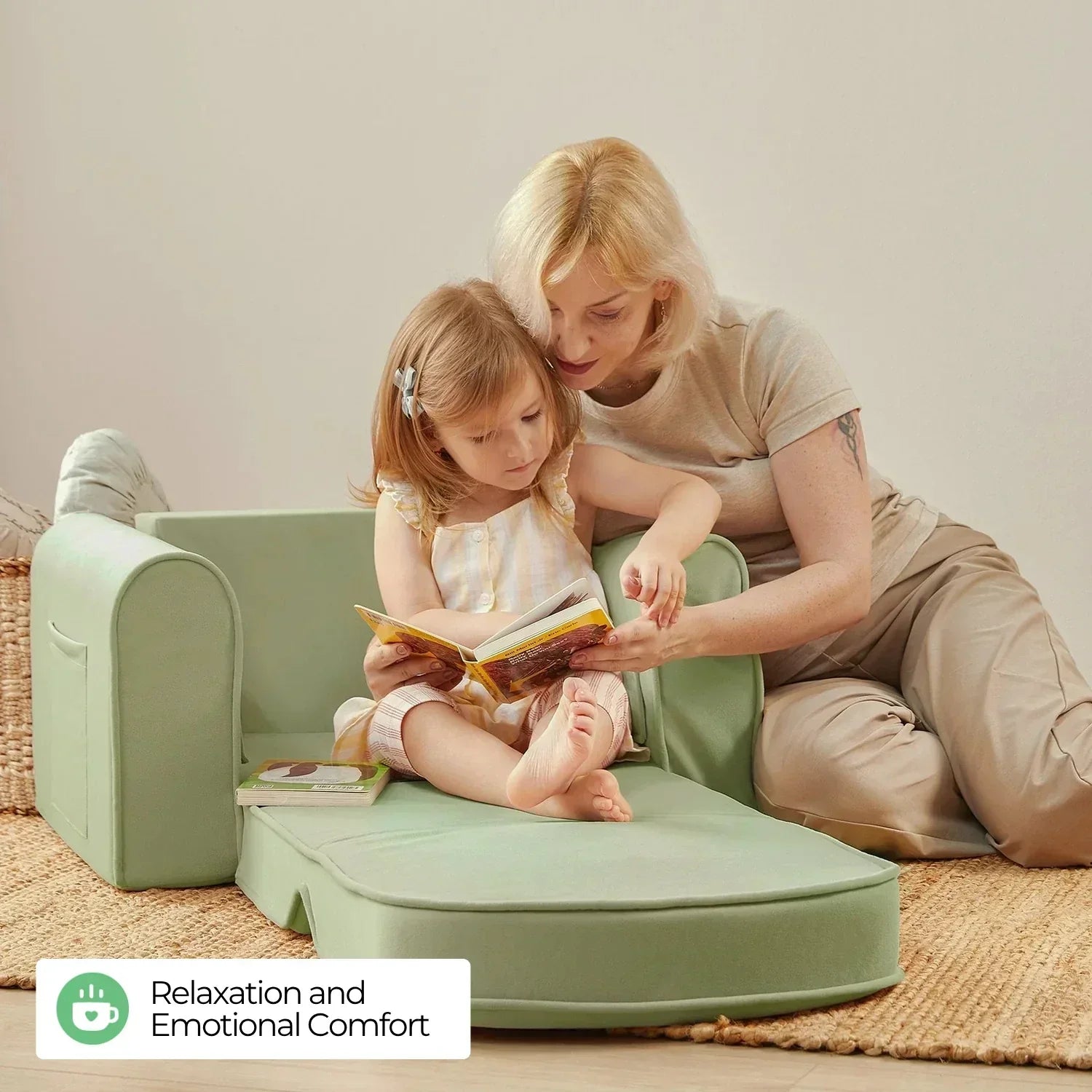 A blonde mom wearing a khaki short-sleeve top and khaki pants sits on the floor, reading with her daughter, who is sitting on a sage-colored sofa.