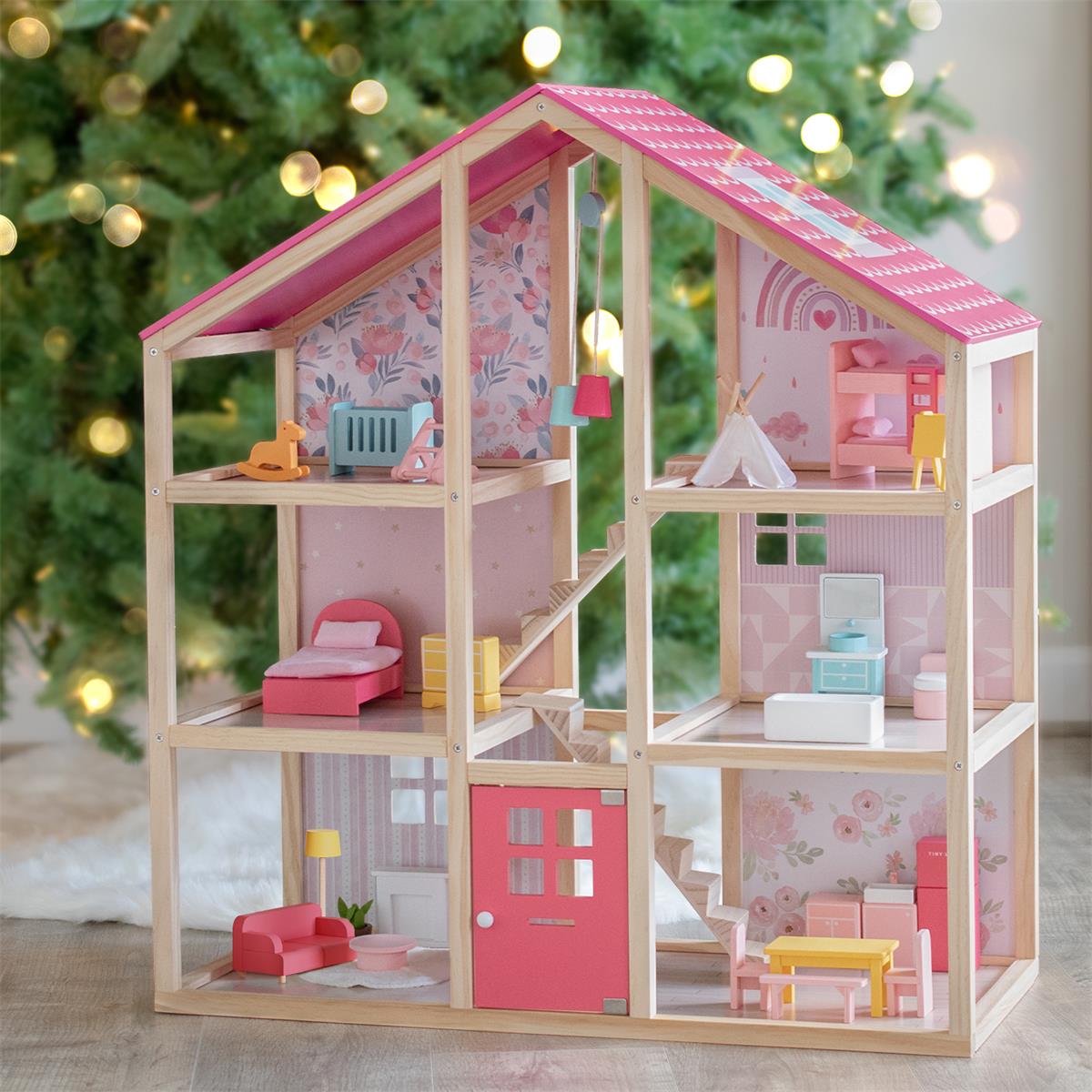 A pink dollhouse filled with colorful toy furniture is placed in front of the Christmas tree.