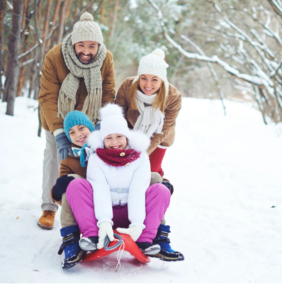 Mom and dad happily sled outdoors with their son and daughter.
