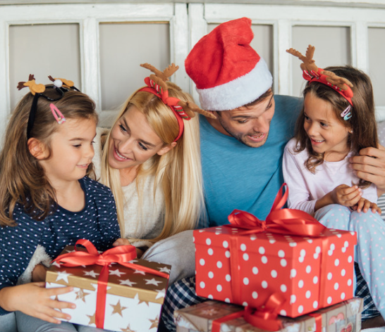 Mom and Dad happily hug their child while giving them Christmas gifts.
