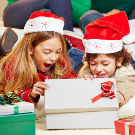 wo kids wearing Christmas hats are excitedly unwrapping their Christmas presents.