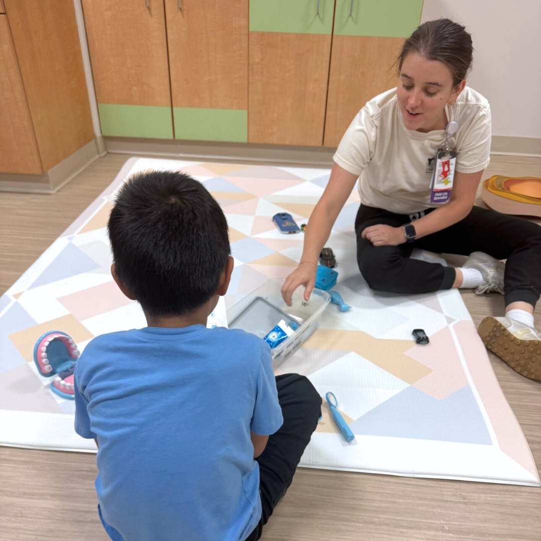 A kind volunteer is gently playing a game with a little boy on the hospital’s play mat.