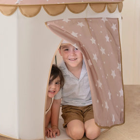 Two young children smile as they peek from the doorway of the Tiny Land® Cheerful Pennant Castle Tent, featuring a pink and white star-patterned curtain and scalloped trim—a delightful indoor playhouse for imaginative fun from Tiny Land.