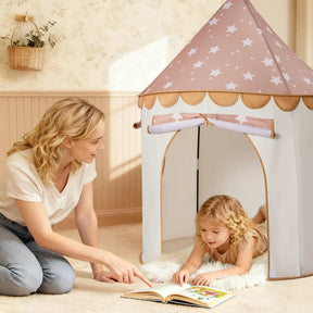 A woman sits on the floor beside a young girl lying on a rug inside the Tiny Land® Cheerful Pennant Castle Tent. She points to an open book, surrounded by soft lighting and light colors in this cozy Tiny Land playhouse scene.