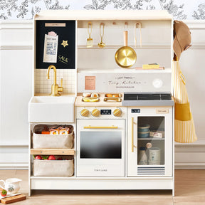 The Tiny Land® BistroSwitch Play Kitchen by Tiny Land features a sink, faucet, stove, oven, pretend fridge, hanging utensils, play food baskets, gold accents, and a chalkboard—perfect for imaginative kids’ pretend play.|White