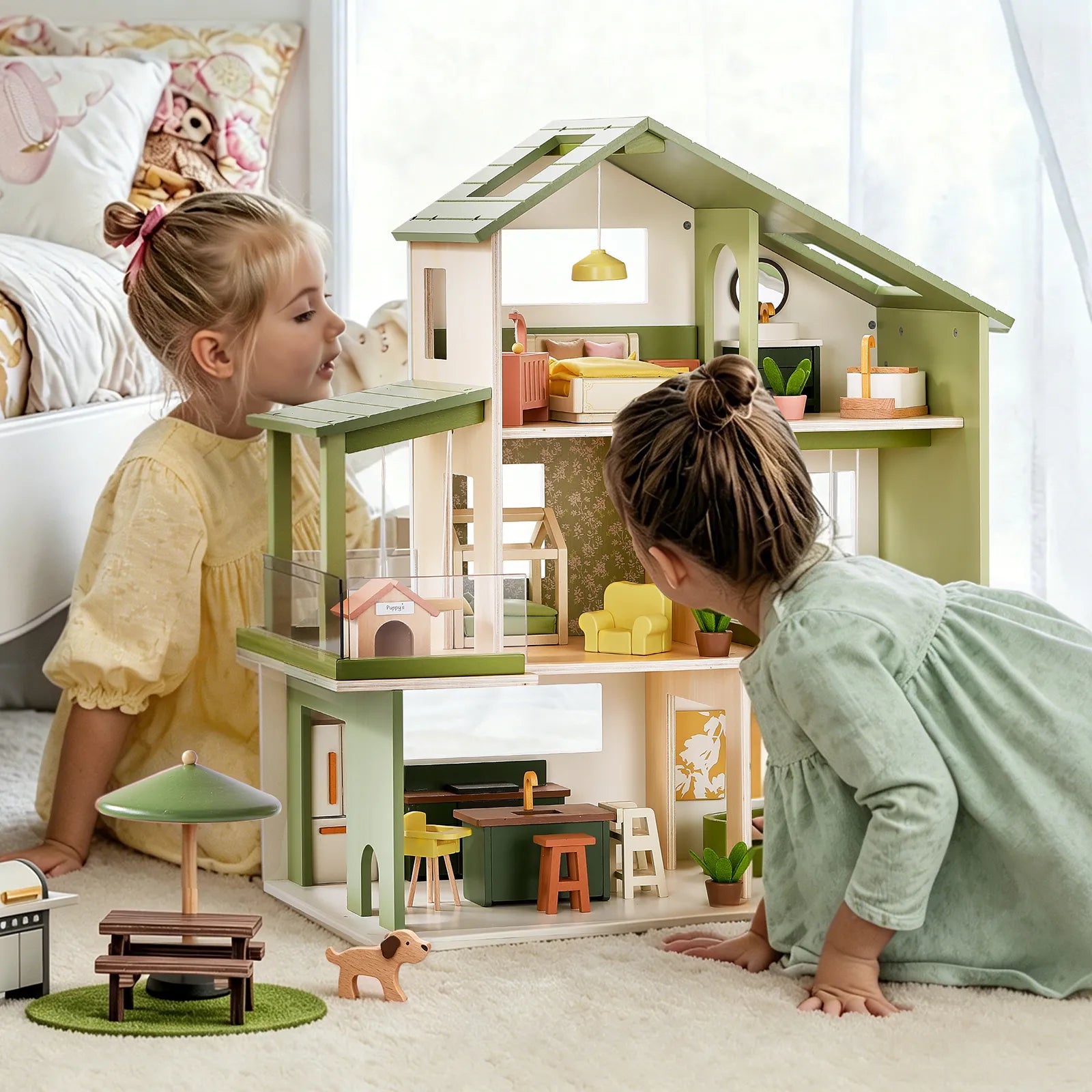Two young girls play with the Tiny Land® Sweetwood Cottage Dollhouse, furnished with miniature furniture. A toy dog and picnic table sit on a play mat nearby as sunlight streams through a window behind them.|Green