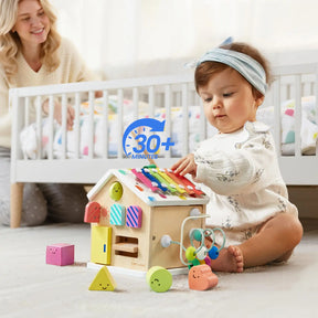 A baby plays with the Tiny Land® Cottage Activity Cube - Rainbow by Tiny Land on the nursery floor, while an adult smiles nearby and a crib sits in the background. A “30+ minutes” playtime graphic appears on the image.