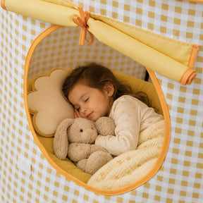 A young child sleeps inside a yellow and white gingham Tiny Land® Kids Tent, hugging a stuffed bunny near a cloud-shaped pillow in their cozy reading nook.|Yellow