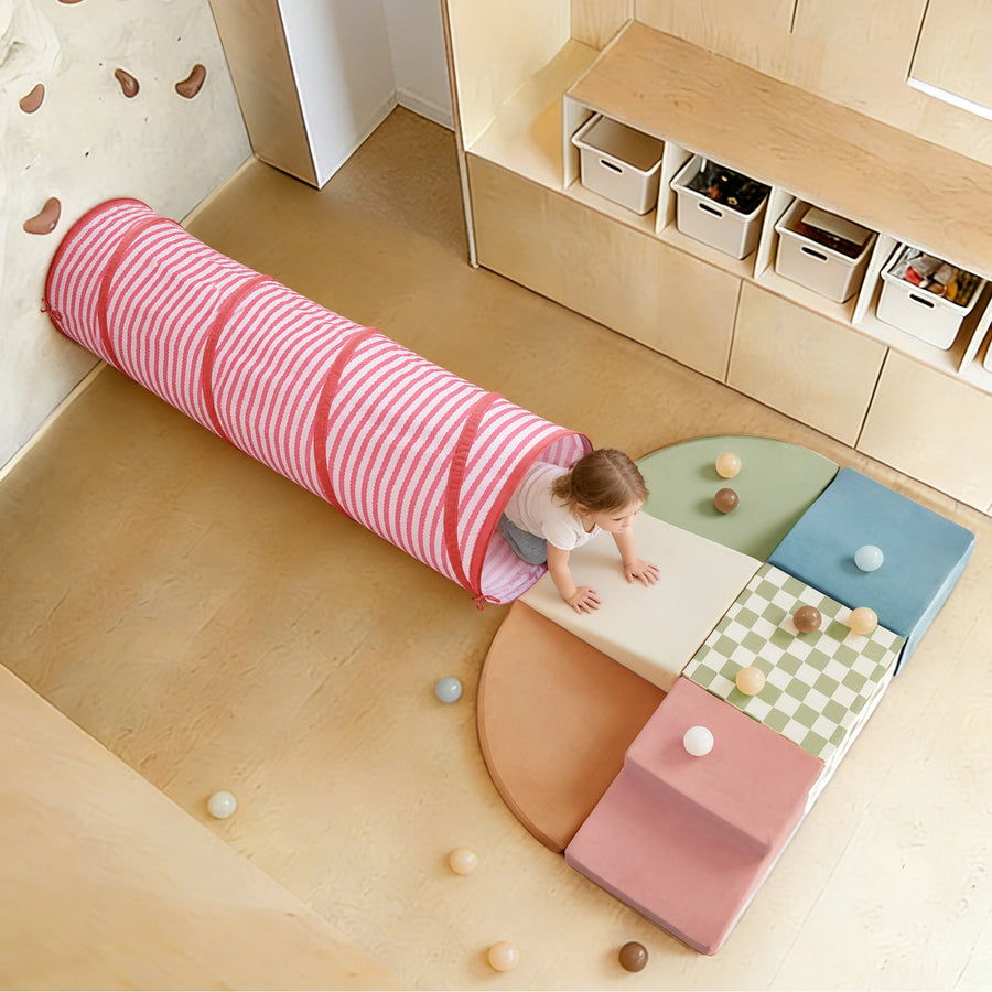 A toddler crawls out of a pink and white striped Tiny Land® Adventure Play Tunnel onto a set of multicolored foam play blocks.|Pink