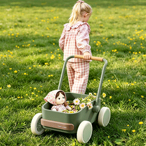 A young girl in pink checkered pajamas pushes the Tiny Land® JoyRide Baby Walker with Blocks by Test across a grassy field, filled with daisies and a doll in a flowery bonnet.