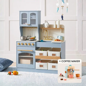 The Tiny Land® Serenity Wooden Kitchen & Coffee Maker playset features a light blue kitchen with cabinets, stove, sink, and storage bins. An inset highlights the coffee maker with cups and accessories for imaginative pretend play fun.