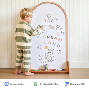 A young child in striped pajamas creates colorful doodles and writes “JOE DREAM LAND” on the Tiny Land® Double-Sided Arched Magnet Chalkboard, using vibrant markers. The playful scene showcases their concentration, emotional comfort, and fine motor skills, highlighted by icons below.