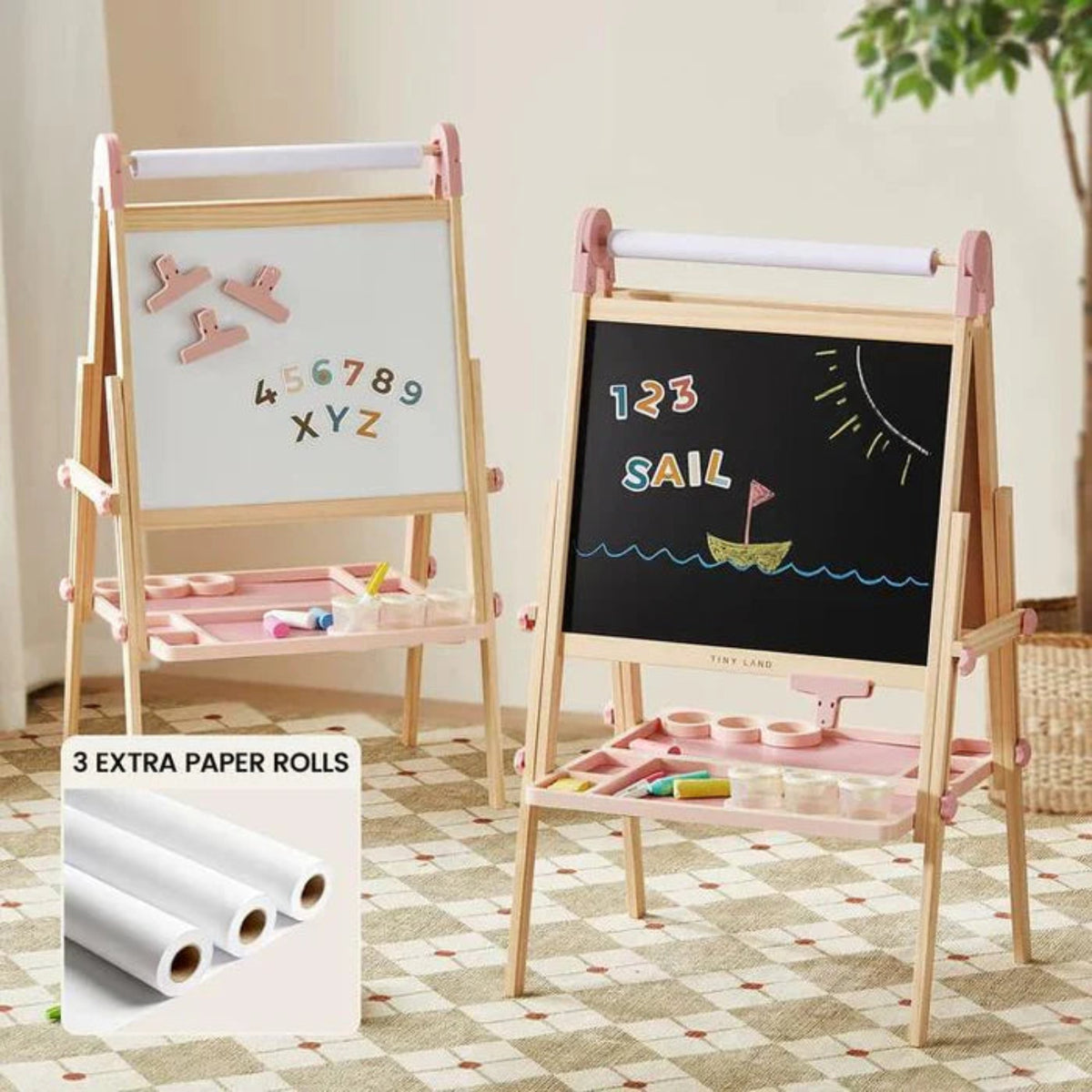 The Tiny Land® Pink Magnitales Easel & Paper Roll Set by Tiny Land features two wooden double-sided easels with pink accents, magnetic whiteboard and chalkboard ("1 2 3 SAIL" boat drawing), art supplies, a paper roll holder, and three extra rolls.