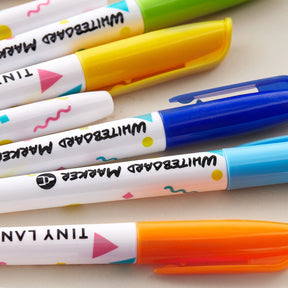 Several colorful markers from the Tiny Land® Magnitales Easel Art Kit with blue, yellow, green, and orange caps rest on a white surface—ideal for kids’ art kits or as part of your Tiny Land creative supplies.