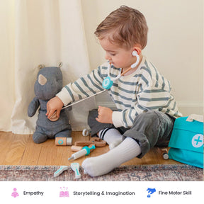 A young child in striped pajamas uses the Tiny Land® Doctor Kit for Kids from Tiny Land to check a stuffed animal with a toy stethoscope, surrounded by child-safe toys and realistic medical supplies. Icons below highlight empathy, storytelling, and fine motor skills.
