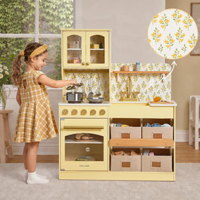 A young girl in a yellow plaid dress enjoys her Tiny Land® Wooden Play Kitchen with Storage for Creative Toddlers, stirring pretend cookware in vibrant pots. This Tiny Land kitchen features floral wallpaper, multifunctional storage bins, and a range of toy appliances—offering endless imaginative fun.|Pale Yellow