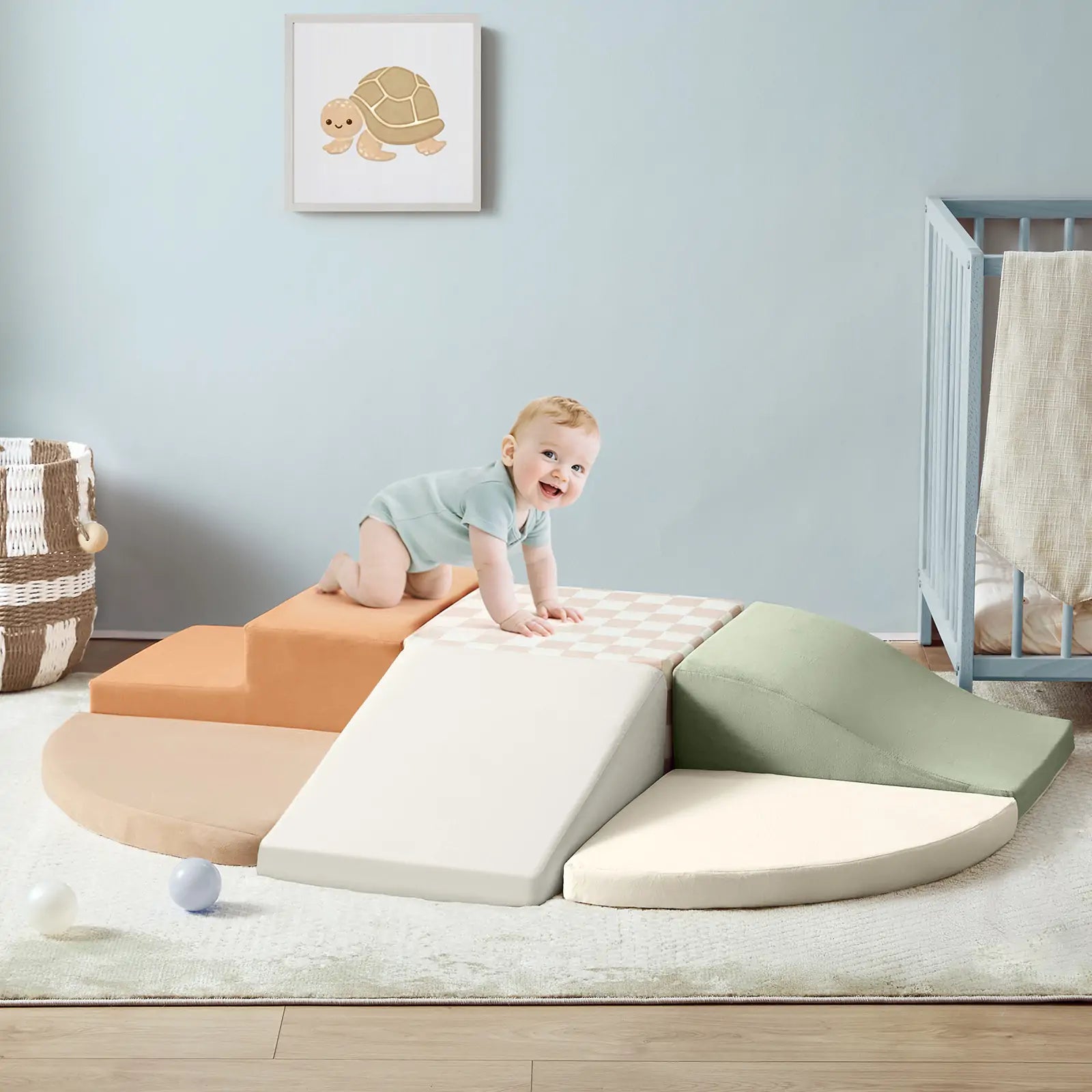 A smiling baby in a light blue onesie climbs on pastel Tiny Land® PlayNest Climbing Blocks, boosting gross motor skills in a cozy nursery with a crib, basket, and turtle wall art.