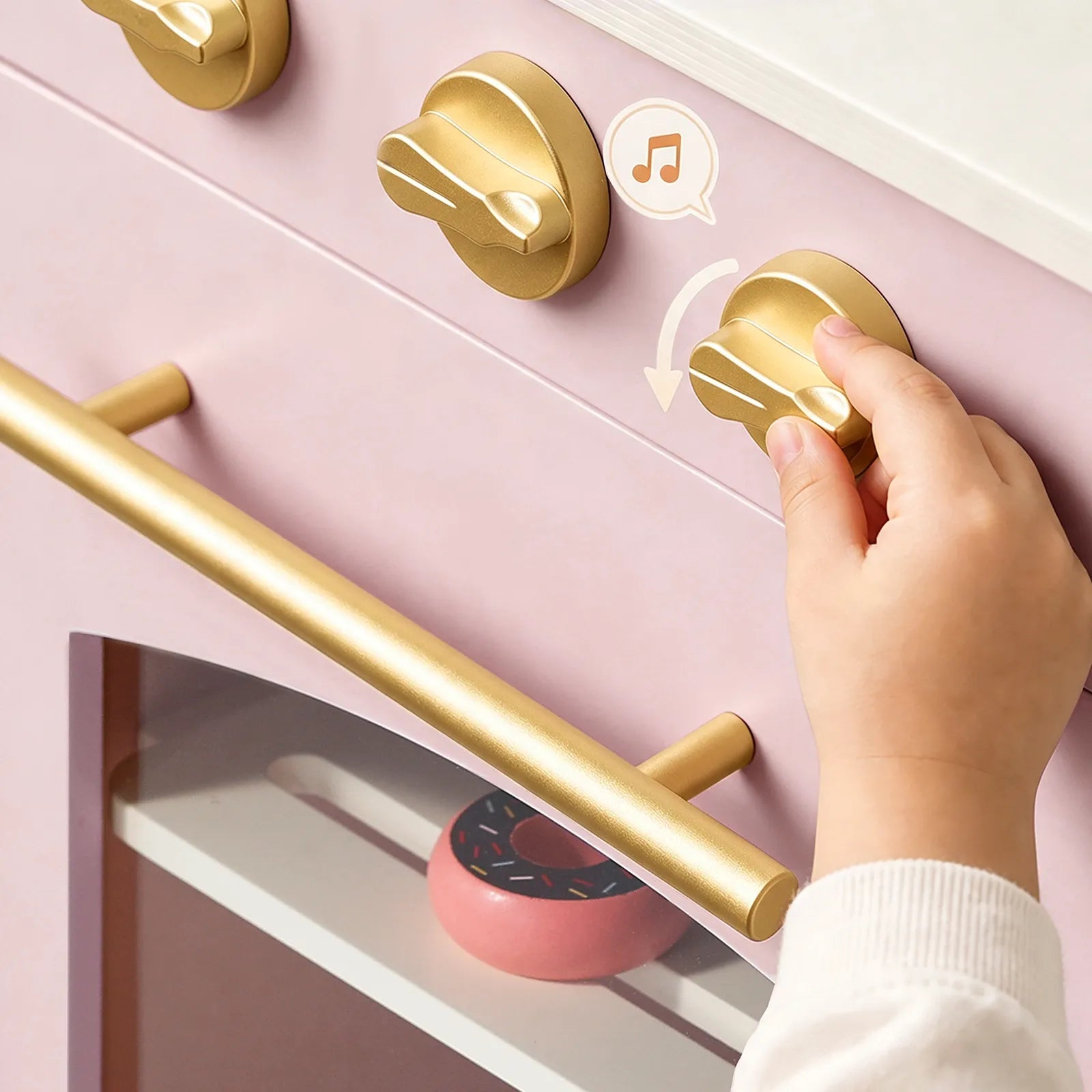 A child’s hand turns a gold oven knob on the Tiny Land® Wooden Play Kitchen with Storage for Creative Toddlers, where pretend cookware and a pink toy donut are visible inside the multifunctional storage oven.|Sakura Pink