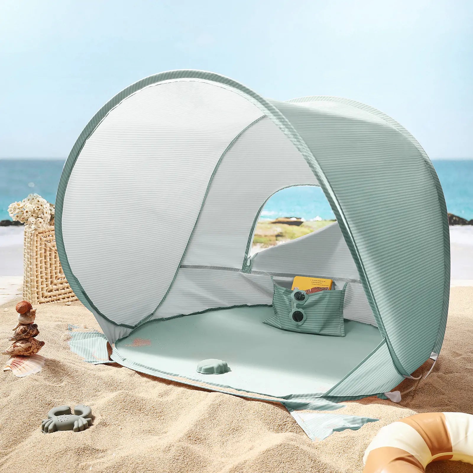 The Tiny Land® One-Stop Beach Toy & Tent Set – Sea Blue by Tiny Land sits on sandy shores, featuring a UV-protective tent with mesh windows, open front, small pillow, plus a sand play set and basket—all against the ocean backdrop.