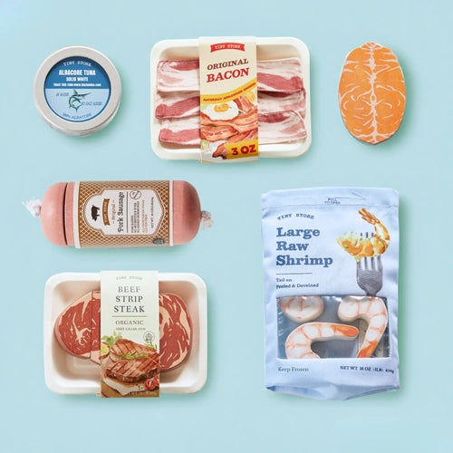 A selection of Tiny Land® Organic Meat & Seafood Pack wooden play foods—including bacon, steak, salmon, shrimp, a tuna can, and sausage—is displayed neatly on a light blue background. Created by Tiny Land for pretend play kitchens, each piece is thoughtfully labeled to replicate real meat and seafood products.