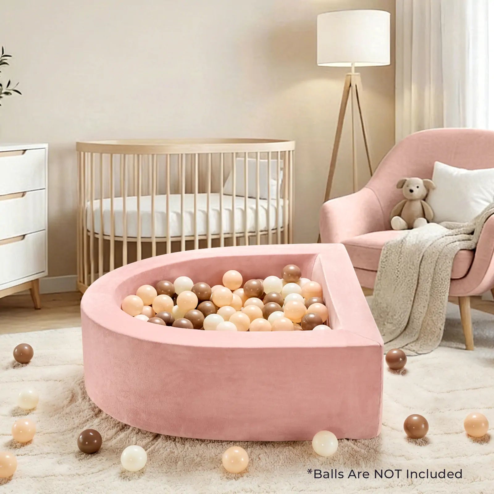A cozy nursery with a Tiny Land® PlayNest Ball Pit (ocean balls not included) in pink, pastel and brown balls, a pink armchair with teddy bear, wooden crib, lamp, and white dresser by Tiny Land in the background.|pink