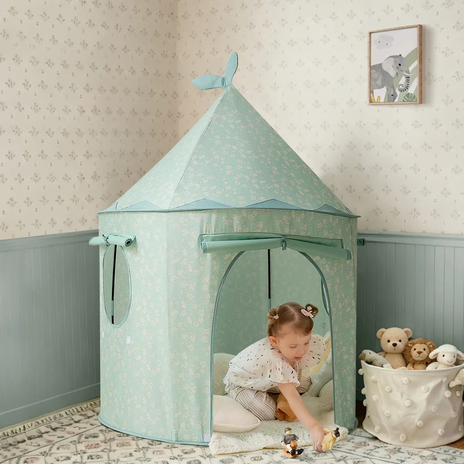 A young child plays with Tiny Land® Tiny Sprout Castle Tent, decorated with white floral patterns, in a cozy room. Plush toys and framed animal art appear in the softly lit background.