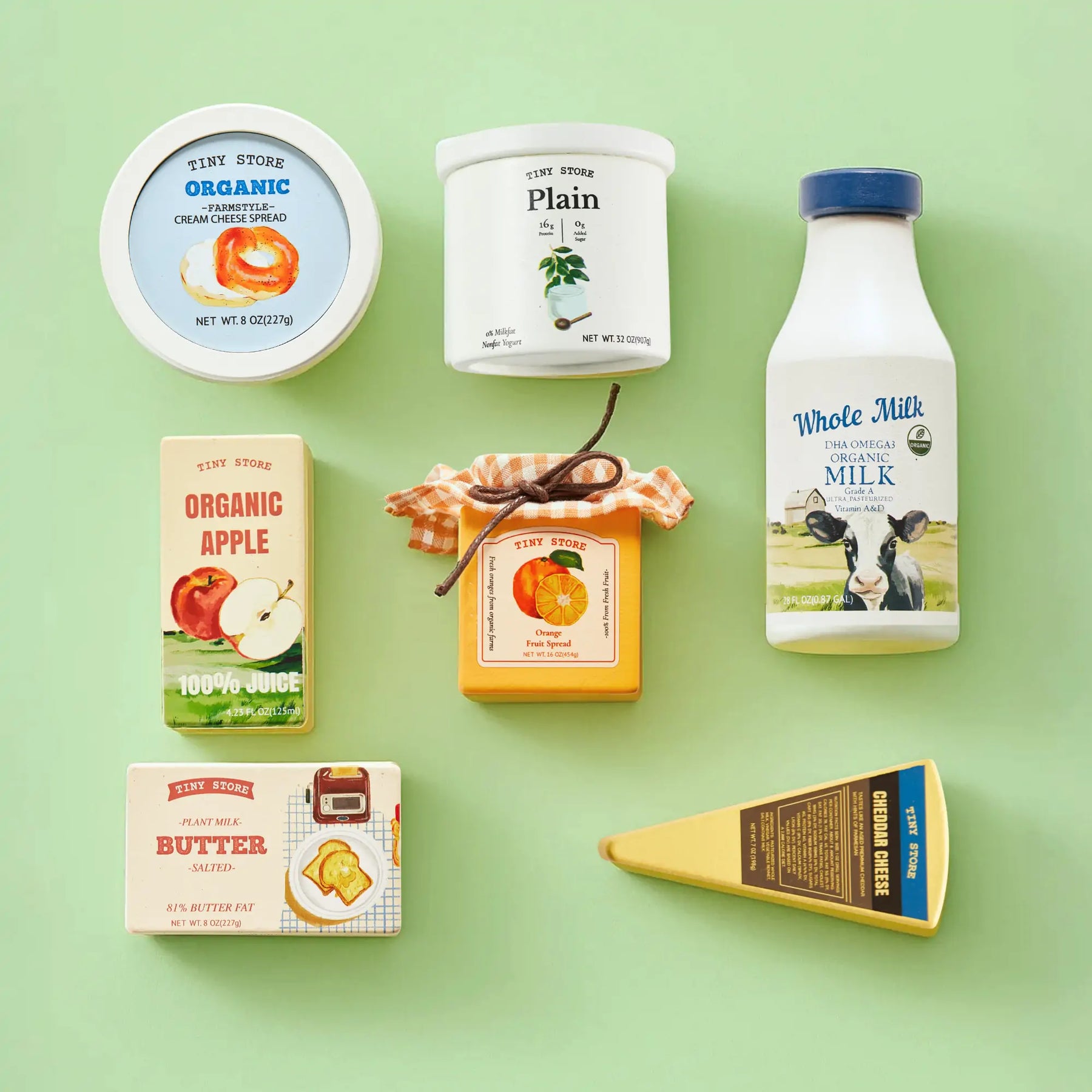 Tiny Land® Organic Play Food - 4 Sets by Tiny Land features assorted pretend foods like milk, cream cheese, yogurt, butter, apple juice, jam, and cheddar—all with colorful vintage-style labels on a light green background for extra charm.