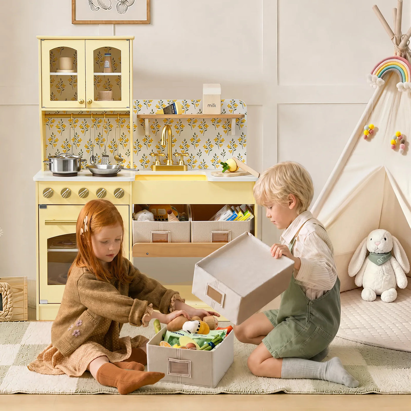 Two young children sit on a rug in a playroom, organizing toys in boxes. In the background, a Tiny Land® Wooden Play Kitchen with Storage for Creative Toddlers, a teepee, and a stuffed bunny from Tiny Land create a cozy and playful atmosphere.|Pale Yellow