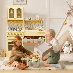 Two young children sit on a rug in a playroom decorated in soft pastel colors, organizing stuffed animals and toys into storage boxes beside the Tiny Land® Wooden Play Kitchen with Storage for Creative Toddlers by Tiny Land and a small tent. Pretend cookware enhances the imaginative atmosphere as they play.|Pale Yellow