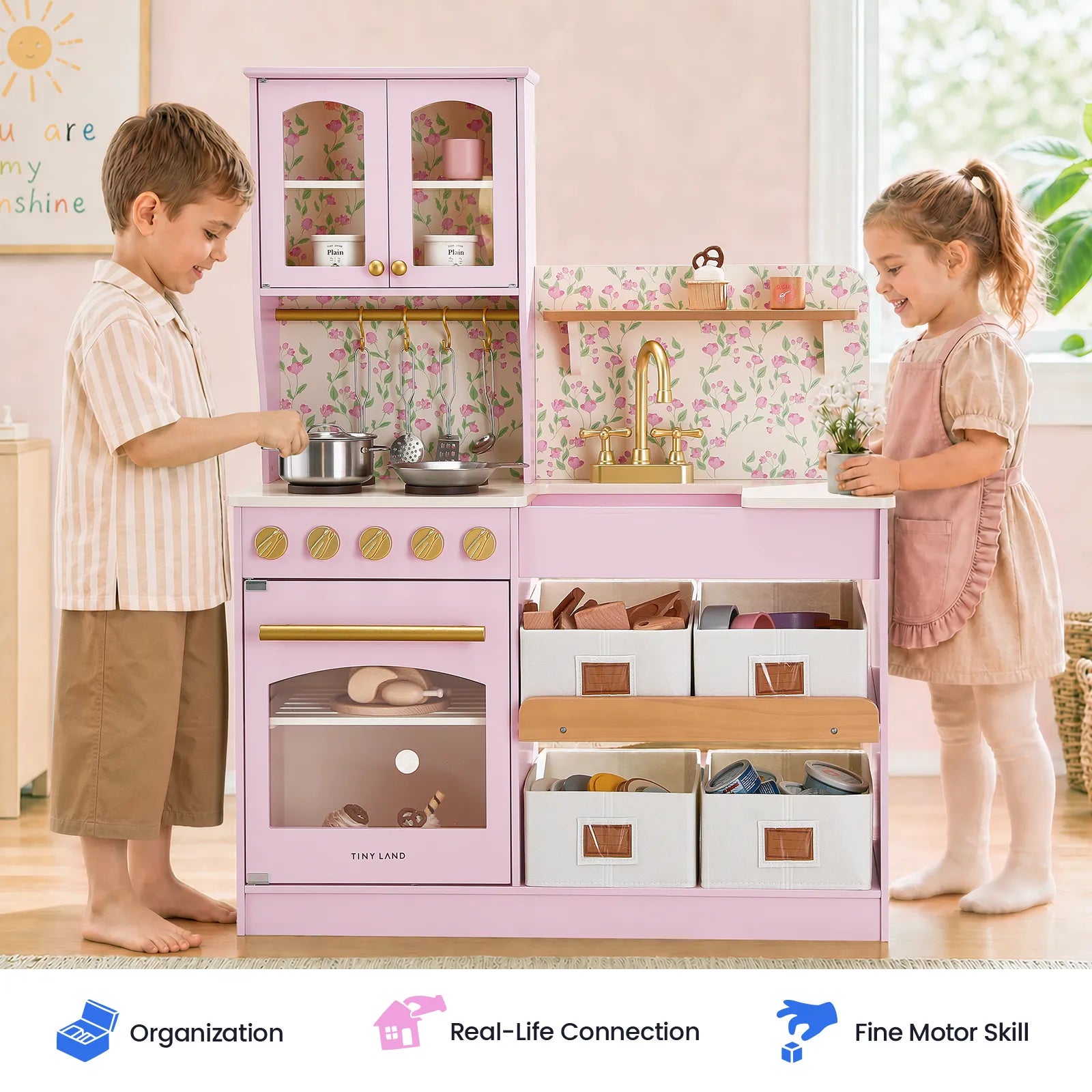 Two young children play with the Tiny Land® Wooden Play Kitchen with Storage for Creative Toddlers, cooking and organizing pretend meals using the included cookware. Spacious storage bins are tucked under the counter of this multifunctional Tiny Land kitchen set. Icons below highlight features such as organization, real-life skill building, and fine motor development.|Sakura Pink