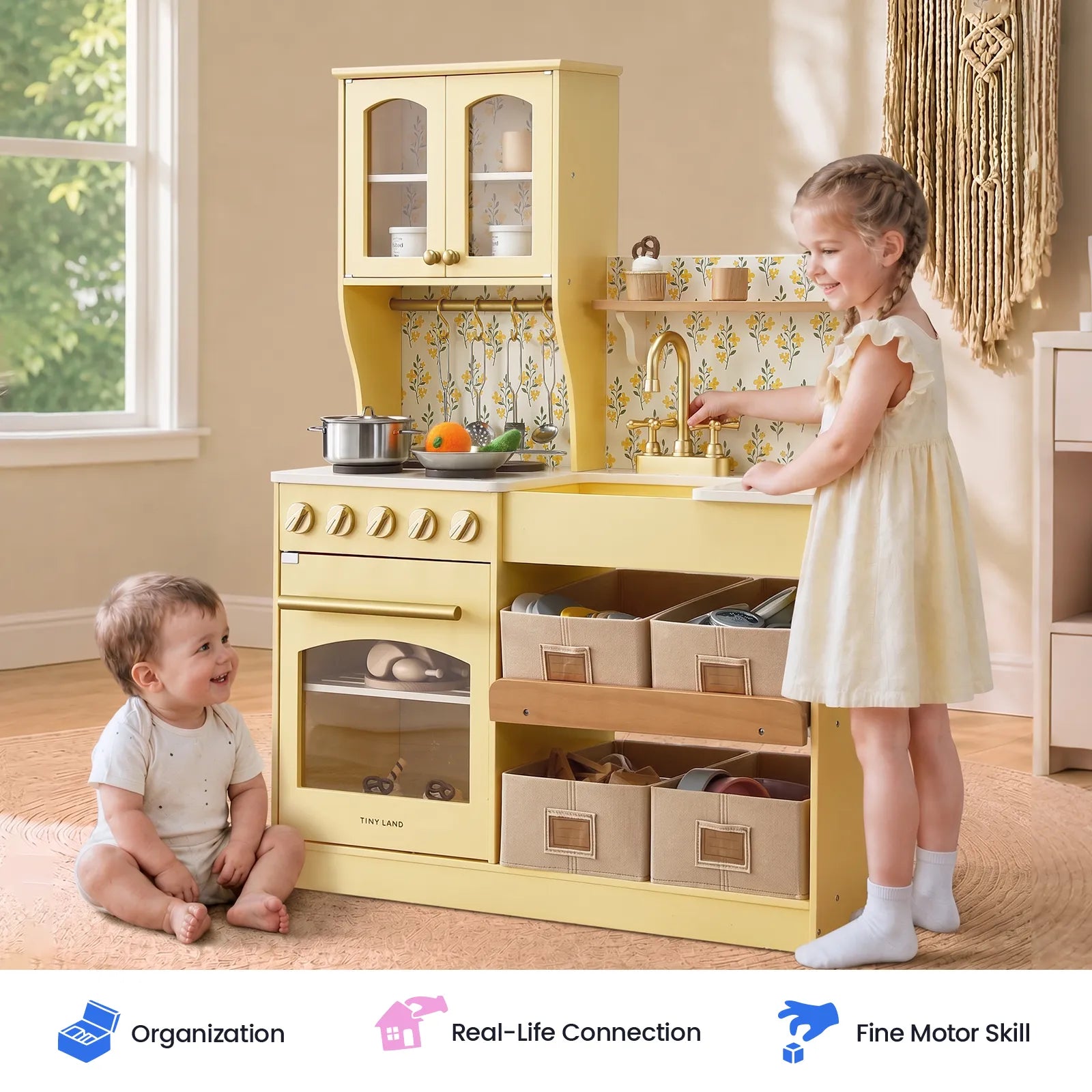 Two young children play with the Tiny Land® Wooden Play Kitchen with Storage for Creative Toddlers in a sunlit room. The older child stands and pretends to wash dishes using the included pretend cookware, while the younger child sits on the floor, smiling.|Pale Yellow