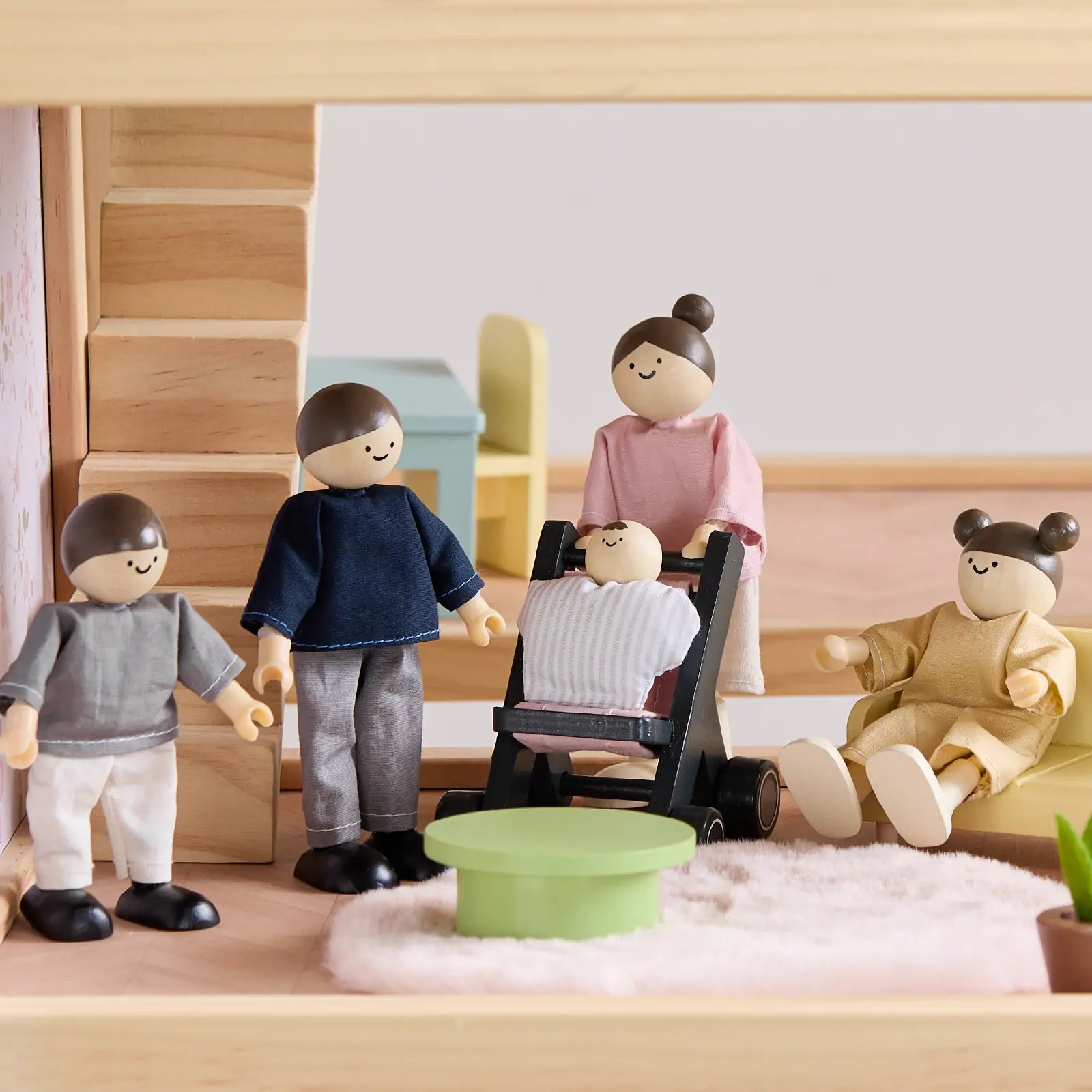 Four Tiny Land® Wooden Dollhouse Dolls and a baby in a stroller from Tiny Land INC are arranged in a cozy living room with natural wood dolls, wooden furniture, and a round green table on a fluffy rug.