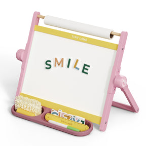 The Tiny Land® Double-Sided Magnetic Tabletop Easel - Pink by Tiny Land is a kids' easel with a whiteboard, colorful magnetic letters spelling “SMILE,” storage trays for art supplies, and a paper roll on top.