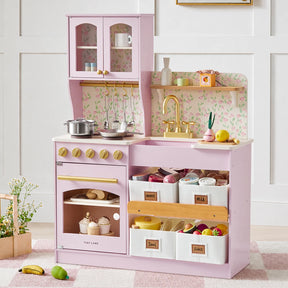 The Tiny Land® Wooden Play Kitchen with Storage for Creative Toddlers by Tiny Land comes in pink with gold accents and includes pretend cookware, toy food, pots, and labeled storage bins for meat, milk, tools, and fruit. Set against floral wallpaper for added charm, this multifunctional play kitchen features a sink, oven, stove, and thoughtful storage—while decorative flowers placed nearby complete the inviting scene.|Sakura Pink