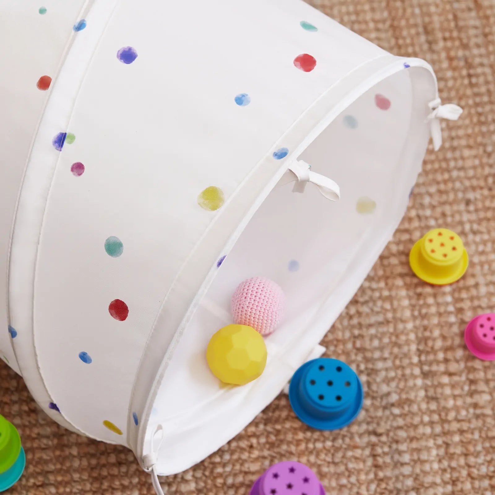 The Tiny Land® Adventure Play Tunnel - Colorful Polka Dots by Tiny Land sits on a brown carpet, surrounded by pink, yellow, blue, and purple toy balls for indoor fun.|white