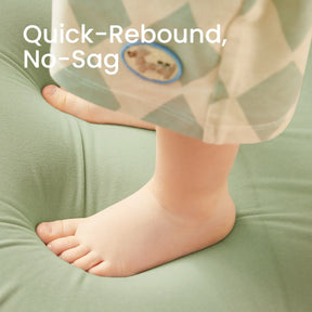 A child's bare feet create a slight dip in the Tiny Land® GentleSnug Kid Chair - Sage, but it springs back fast, highlighting its quick-rebound and no-sag qualities. Text: Quick-Rebound, No-Sag. Brand: Tiny Land.
