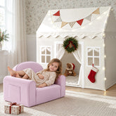 A young girl relaxes in a light purple GentleSnug Kid Chair in front of a Tiny Land® Cozy Nook – Playhouse Tent decorated with a festive wreath, bunting, and string lights.|White