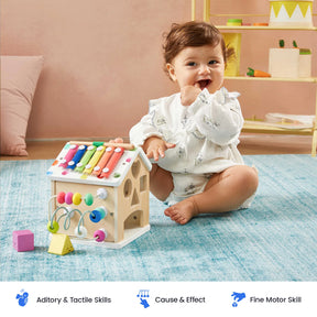 A baby sits on a blue rug, playing with the Tiny Land Rainbow Baby Walker & Activity Cube Developmental Playset, exploring its engaging features. The room is bright with pastel decor. Icons below highlight auditory, tactile, cause and effect, and fine motor skill benefits.