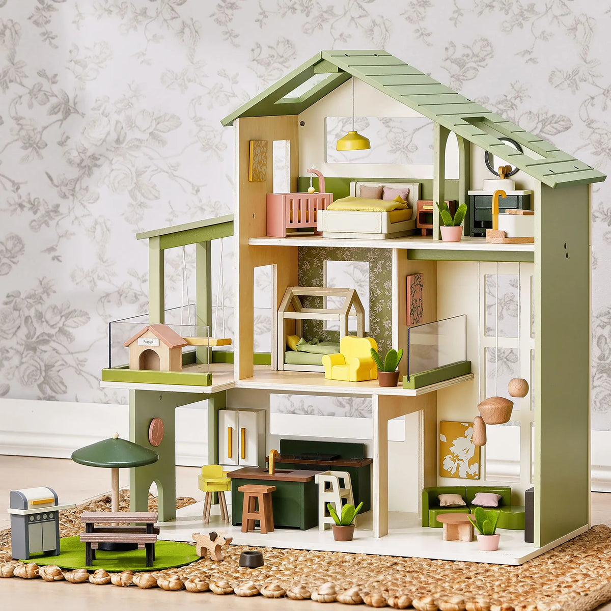 The Tiny Land® Sweetwood Cottage Dollhouse by Tiny Land is a modern wooden dollhouse with three floors, a green roof, miniature furniture, plants, a dog house, patio set, barbecue grill, and floral wallpaper background.|Green