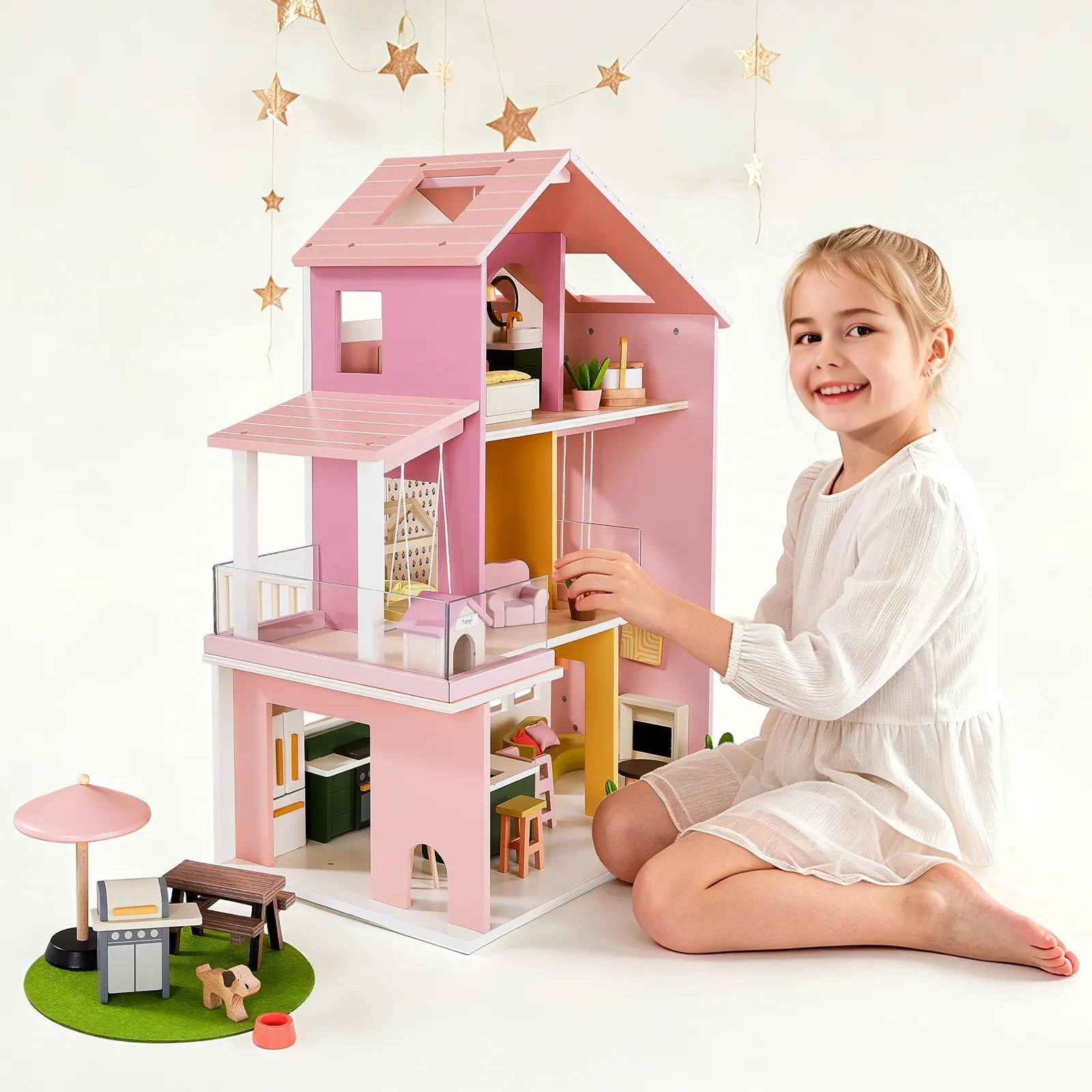 A young girl sits on the floor engaged in imaginative play with a Tiny Land® Sweetwood Adventure Dollhouse & Play Tunnel Set, featuring a multi-level wooden dollhouse and an outdoor grill play set.