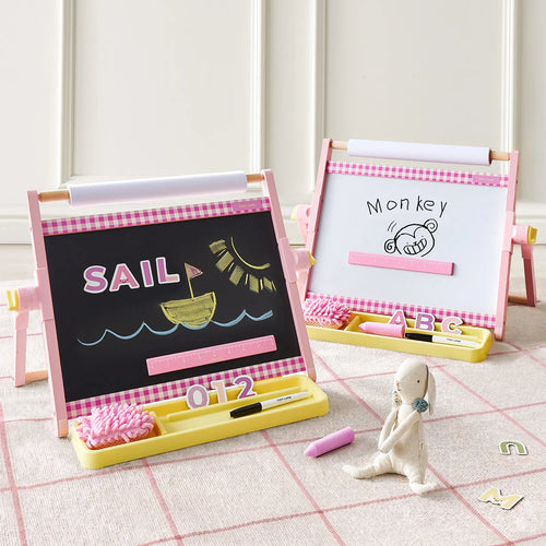 Two pink-framed Tiny Land® Double-Sided Magnetic Tabletop Easels by Tiny Land—each serving as a vibrant kids' art station—display drawings: one featuring a sun, sailboat, and the word 
