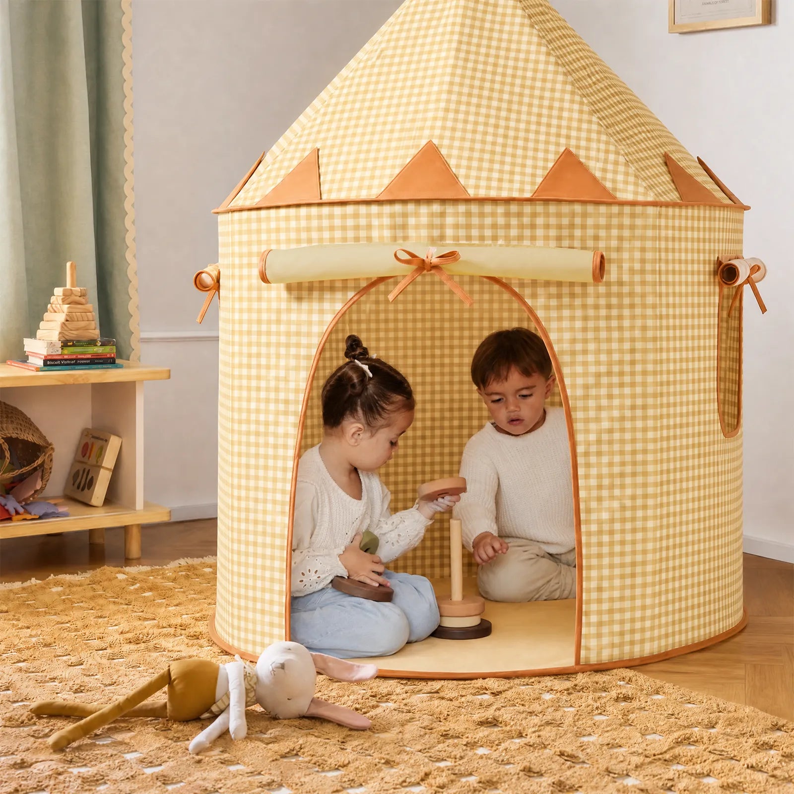 Two young children play with wooden toys inside the Tiny Land® Kids Tent – Indoor Tent for Toddlers by Tiny Land INC. A soft doll and toy blocks are on the carpeted floor, surrounded by warm decor and a wooden shelf holding more toys in the background.